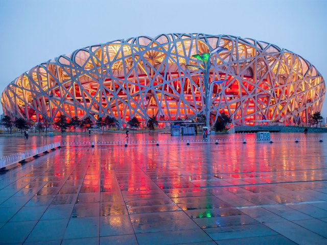The massive Bird's Nest stadium, featuring slender metal bars on the exterior, lit up with red lights