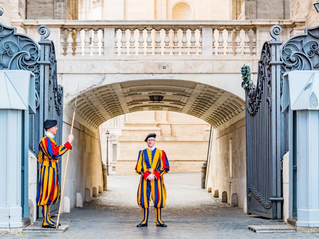 Members of Swiss Guard in blue and yellow uniforms standing under Vatican archway