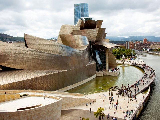 A picture of the gleaming metal exterior of the Guggenheim Museum next to the water