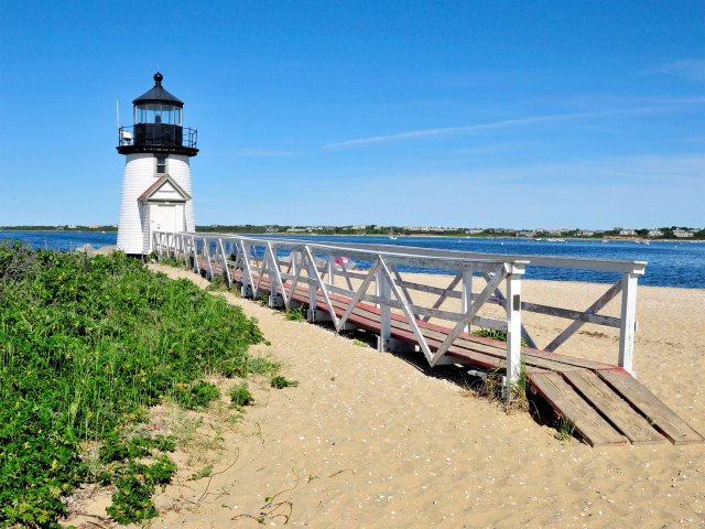 Wooden pathway leading to lighthouse on sandy shoreline of Nantucket Island