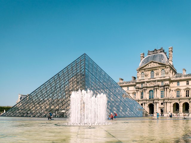 Fountain in front of glass pyramid and exterior of Louvre Museum in Paris, France