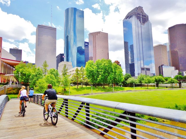 Cyclists on bridge in Houston city park with skyscrapers in background