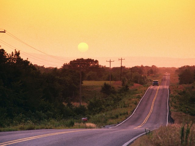 Sole car on hilly two-lane highway in Oklahoma at sunset