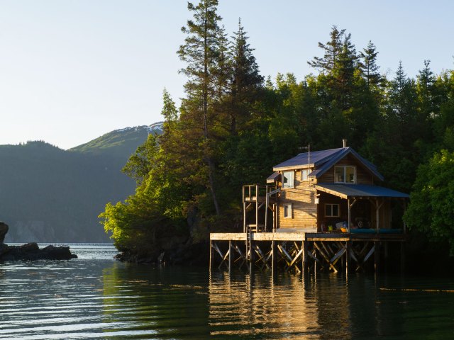 A picture of a home on stilts built into a lake backed by pine trees