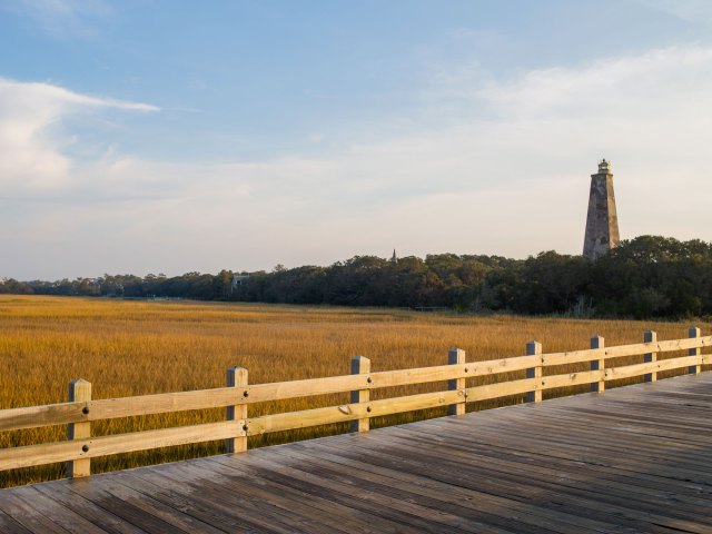 A picture of a wide dock with a tall lighthouse in the background