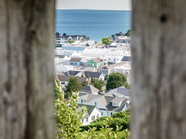 A view through two wooden slats of quaint colorful homes backed by water