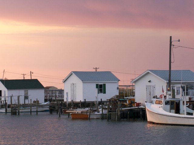 Several small, white wooden homes set next to docks at which several boats sit
