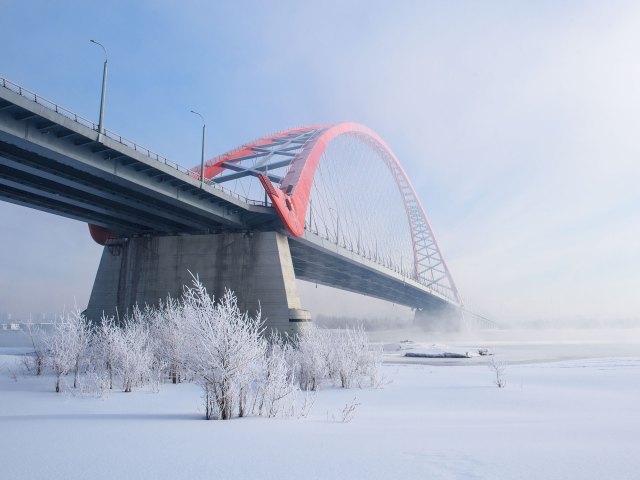 A picture of a large stone bridge with a red arch crossing a frozen, snow-covered lake