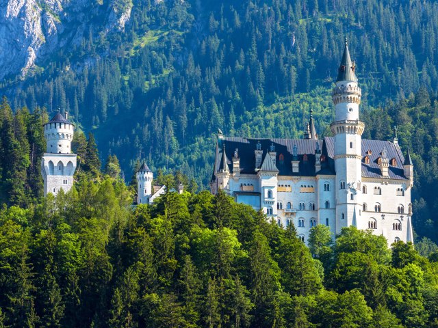 Neuschwanstein Castle in Germany surrounded by forest-covered mountains