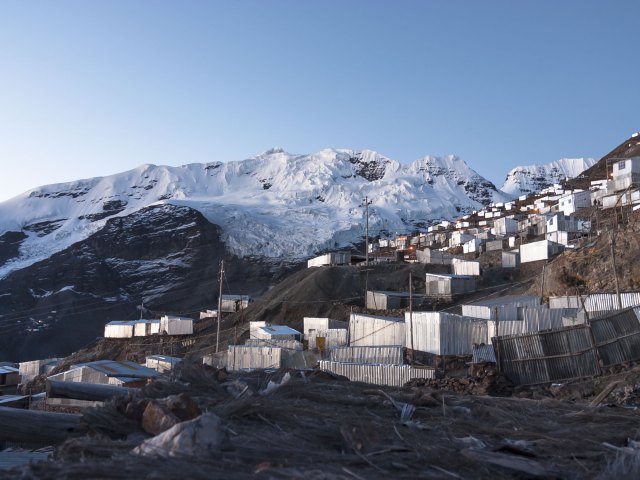 Aluminum-sided buildings built on partially snow-covered mountainside in La Rinconada, Peru