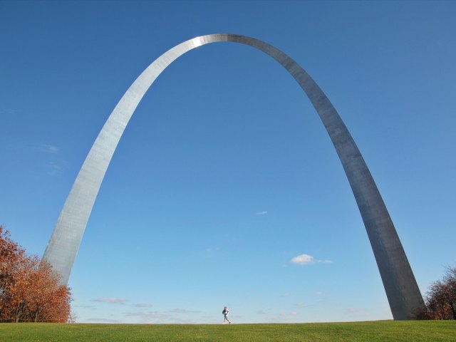 A picture of a man running underneath the Gateway Arch on a sunny day