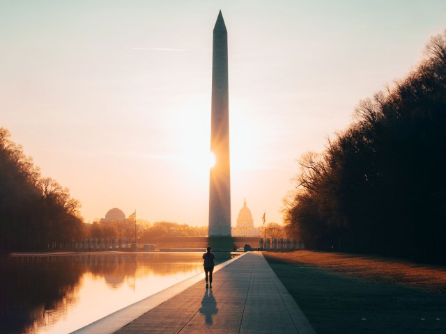 A picture of a man walking alongside the reflecting pool leading up to the Washington Monument at sunset