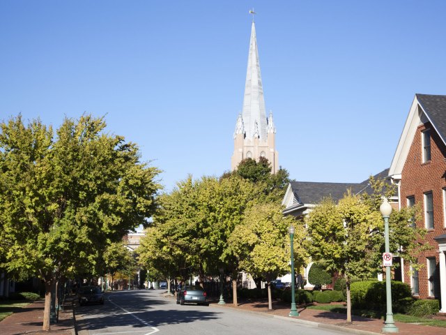 A tall steeple overlooking several red brick homes on a tree-lined street