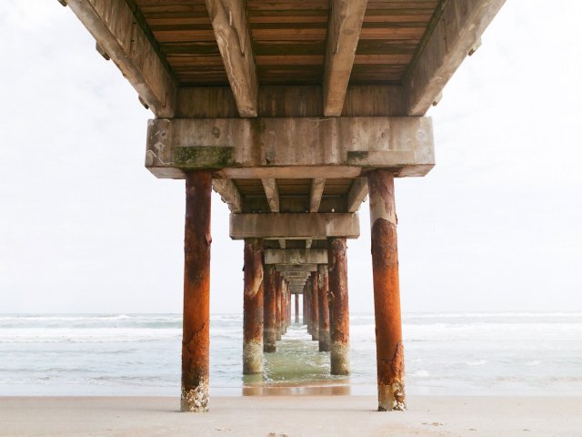 A picture of the underside of a long dock stretching into the ocean from the beach