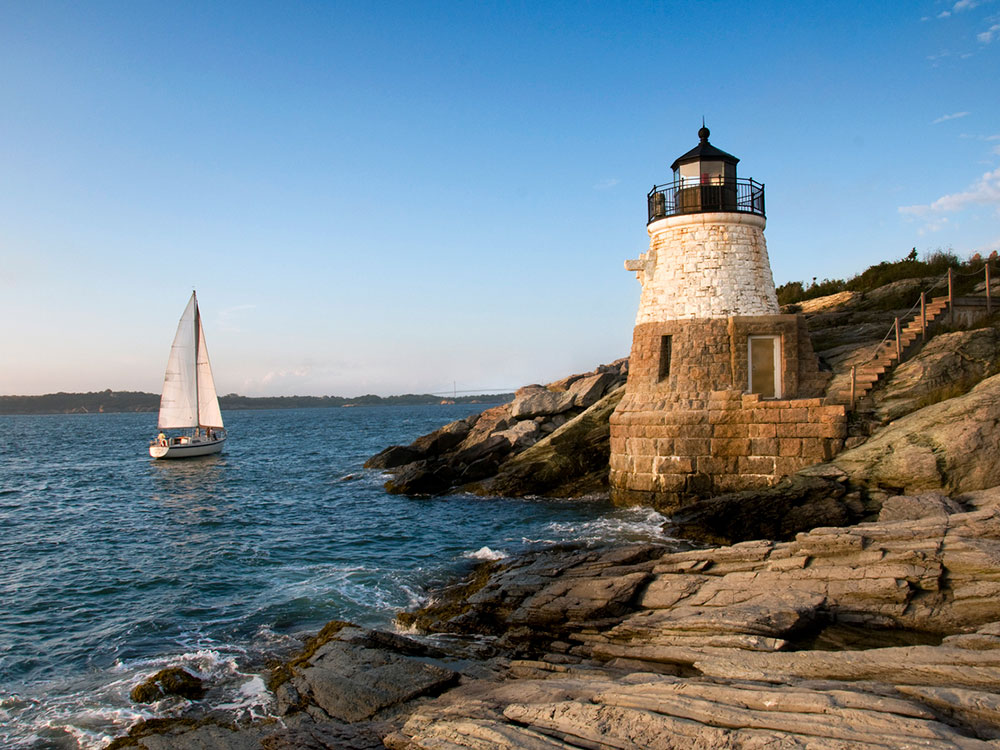 A sailboat on the ocean close to shore where a lighthouse stands
