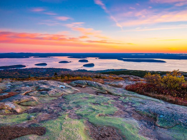 A view from the top of a mountain showing small islands in a bay against a bright sunrise