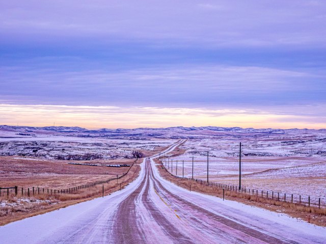 Empty snow-covered road through hilly Wyoming landscape