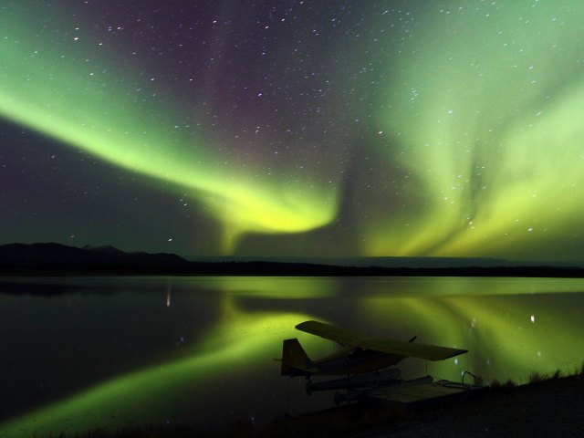 View of northern lights over seaplane parked along lake at night in Alaska
