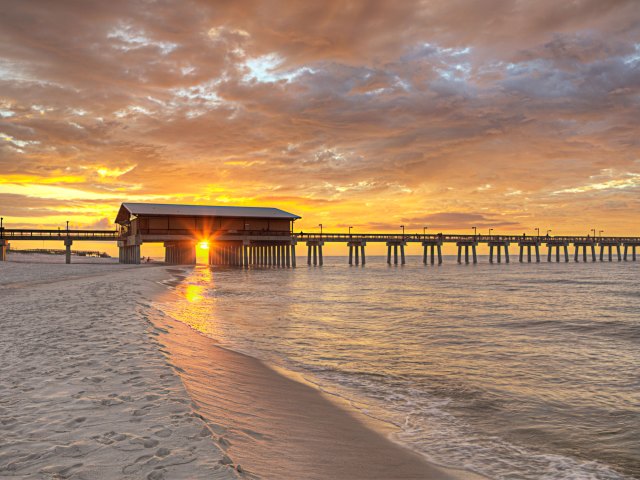 Pier extending from sandy beach over Gulf Coast in Alabama at sunset