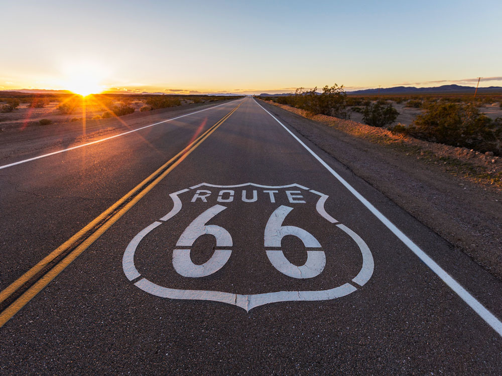 Route 66 sign painted on empty roadway at sunset