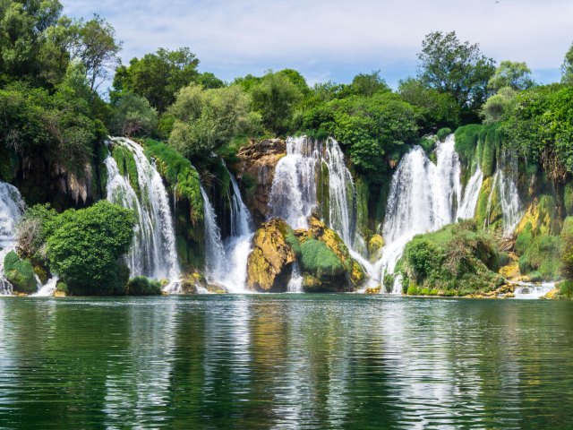 Kravice Waterfalls in Bosnia and Herzegovina, seen from across clear lake