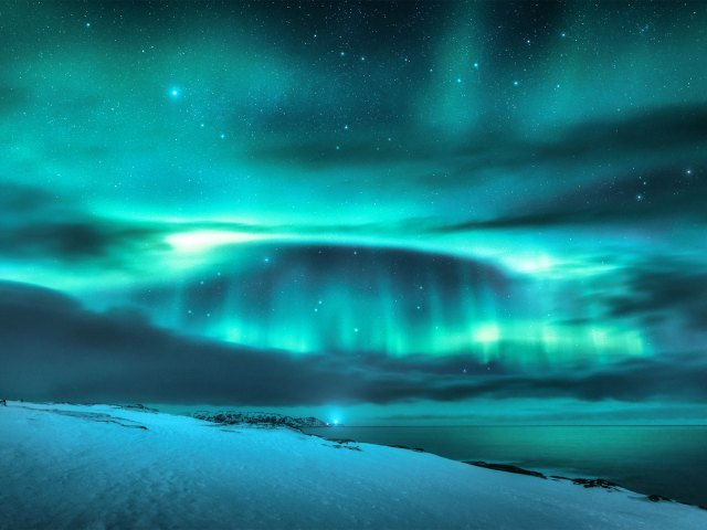 Greenish-blue lights shining above winter landscape in Norway