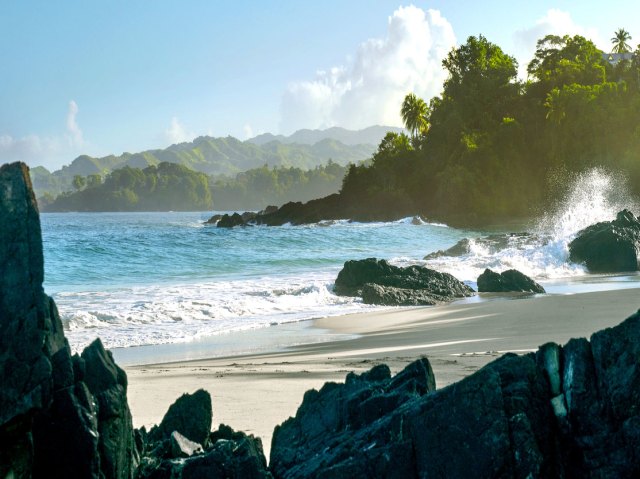 Waves crashing on sandy beach surrounded by boulders in Trinidad and Tobago