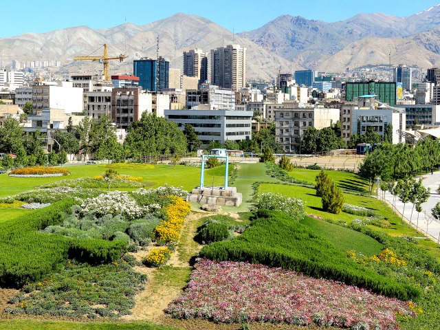Overview of park in Tehran, Iran, with skyscrapers and mountains in background
