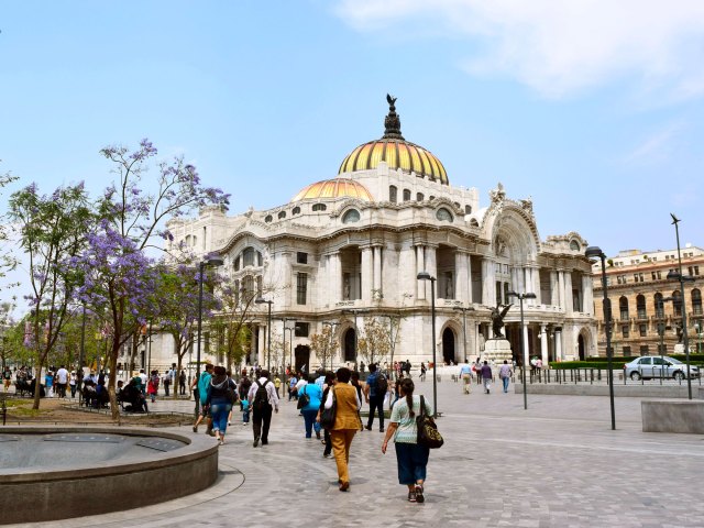 People walking in square fronted by ornate gold-domed building in Mexico City
