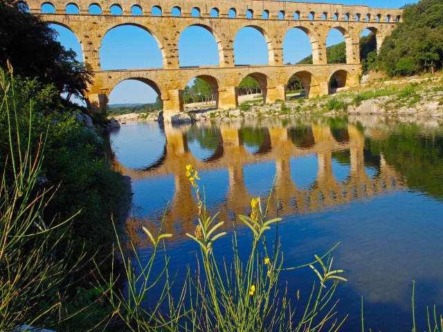 Three-tiered Pont du Gard aqueduct bridge in France, seen from across riverbank