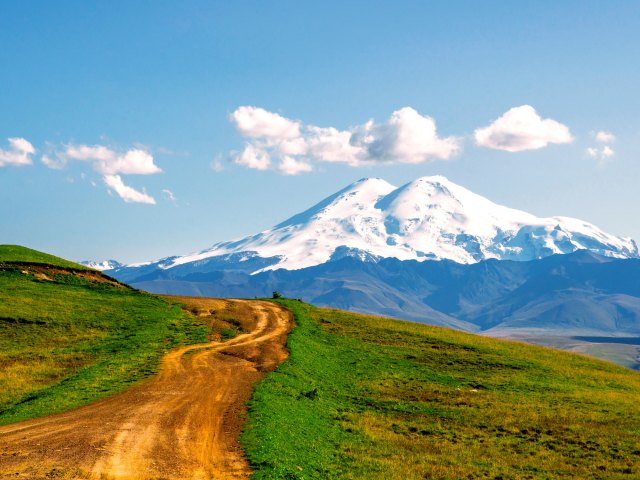 Dirt path leading to snow-covered Mount Elbrus in the distance