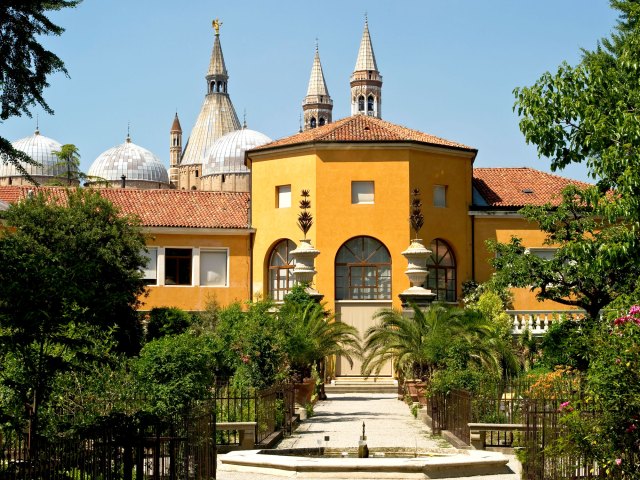 Fountain and tree-lined pathway leading to yellow building at Orto Botanico di Padova, Italy