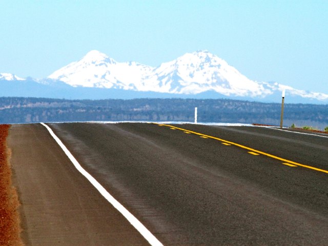 Close-up view of roadway on U.S. Route 20 with snow-capped mountains in the distance