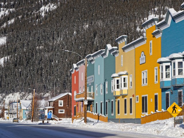 Colorful row homes next to forest-covered mountain in Dawson City, Yukon Territory
