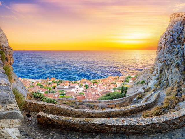 View of Monemvasia, Greece, between steep cliffs with ocean and sunset in background