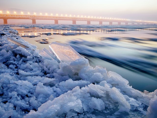 Close-up of icy shoreline and bridge along Trans-Siberian highway in the distance