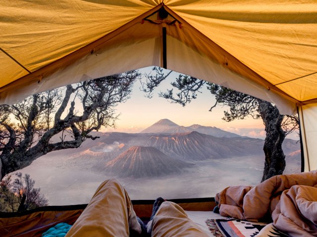 Camper relaxing in tent with view of Indonesian volcano