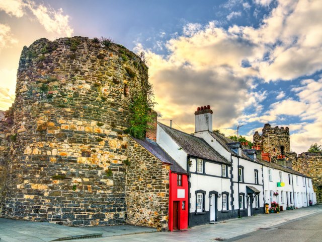 Image of Great Britain's Smallest House, painted bright red and tucked between stone wall and other row homes 