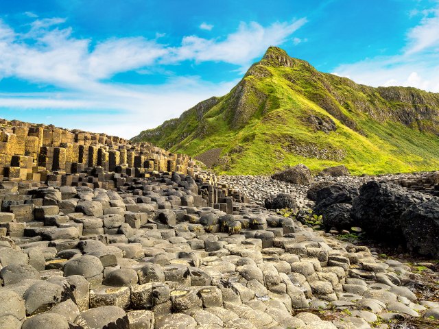 Columns of basalt along Northern Ireland's Giant's Causeway with green hills in background