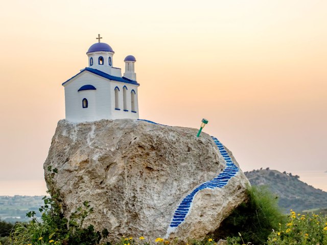 Blue-and-white church on rocky hilltop in Greece at sunset