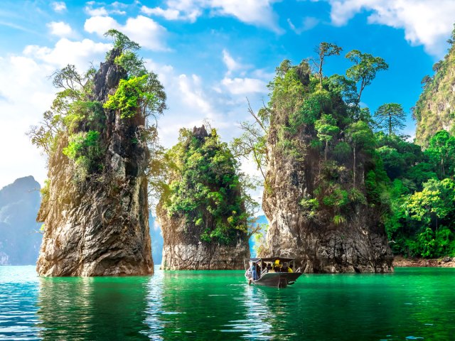 Boat in greenish waters with limestone islands in Thailand