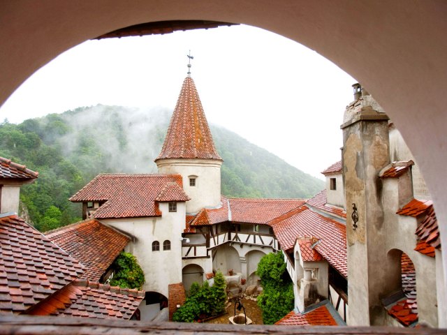 View of Romania's Bran Castle through archway and fog-shrouded mountains