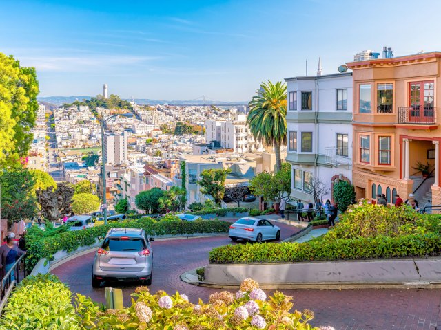 Cars descending windy Lombard Street with view of San Francisco cityscape in background