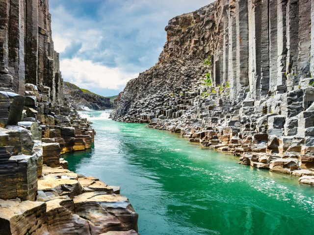 Greenish waters flowing through dramatic Studlagil Canyon in Iceland