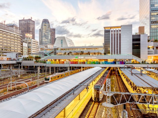 Overhead view of trains, platforms, and Tokyo skyline at Shinjuku Station