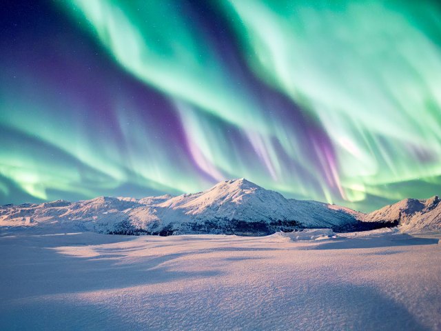 Greenish-blue display of the northern lights over snowy mountain landscape