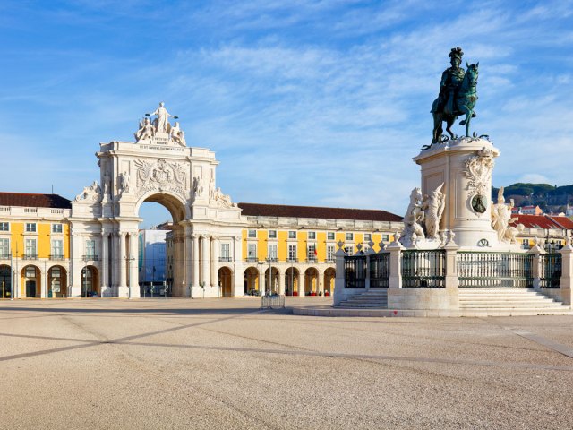 Statue in the center of Praça do Comércio in Lisbon, Portugal, flanked by yellow buildings and grand archway