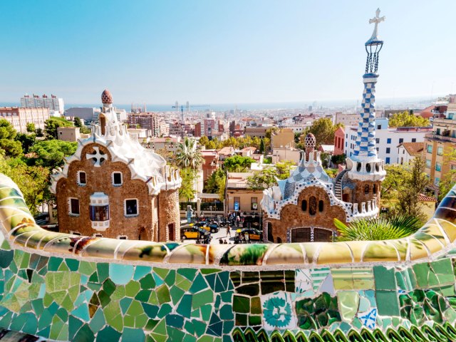 Mosaic-covered wall and buildings overlooking Barcelona skyline at Parc Güell