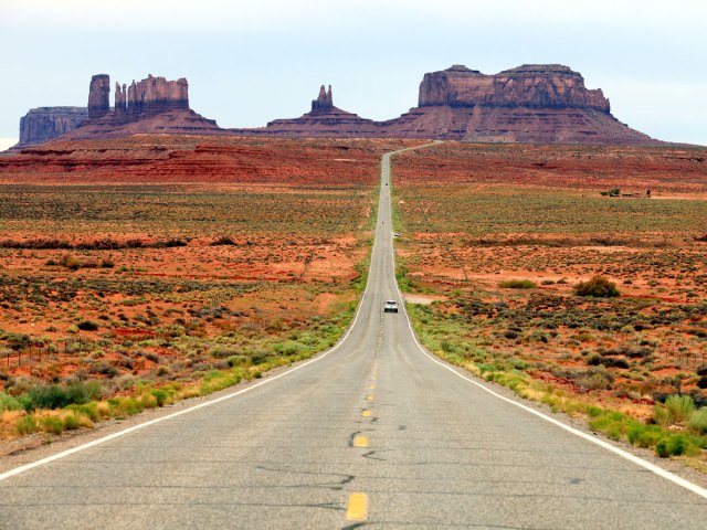 Lone car on Highway 163 driving toward sandstone rock formations across desert