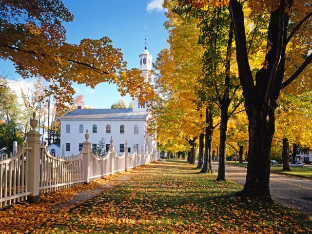 White church in Vermont with sidewalk covered in fallen yellow leaves